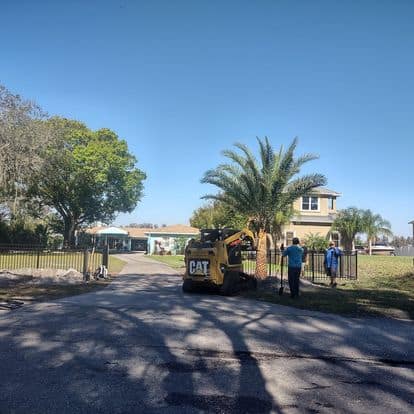 Landscaping crew from Absolute Outdoors LLC working near a palm tree with a mini loader, illustrating their efficient property enhancement services in Odessa, FL.